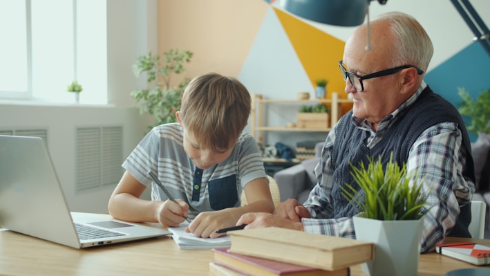 Grandfather helps grandson with homework at desk.