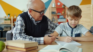 Grandfather helps grandson with homework at desk.