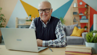 Smiling elderly man with glasses at laptop computer.