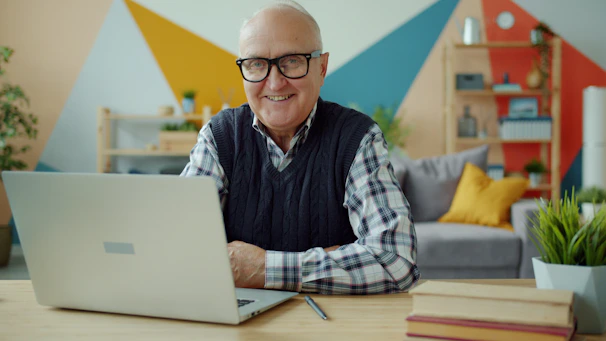 Smiling elderly man with glasses at laptop computer.