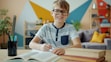 Smiling boy wearing glasses studying at a desk.