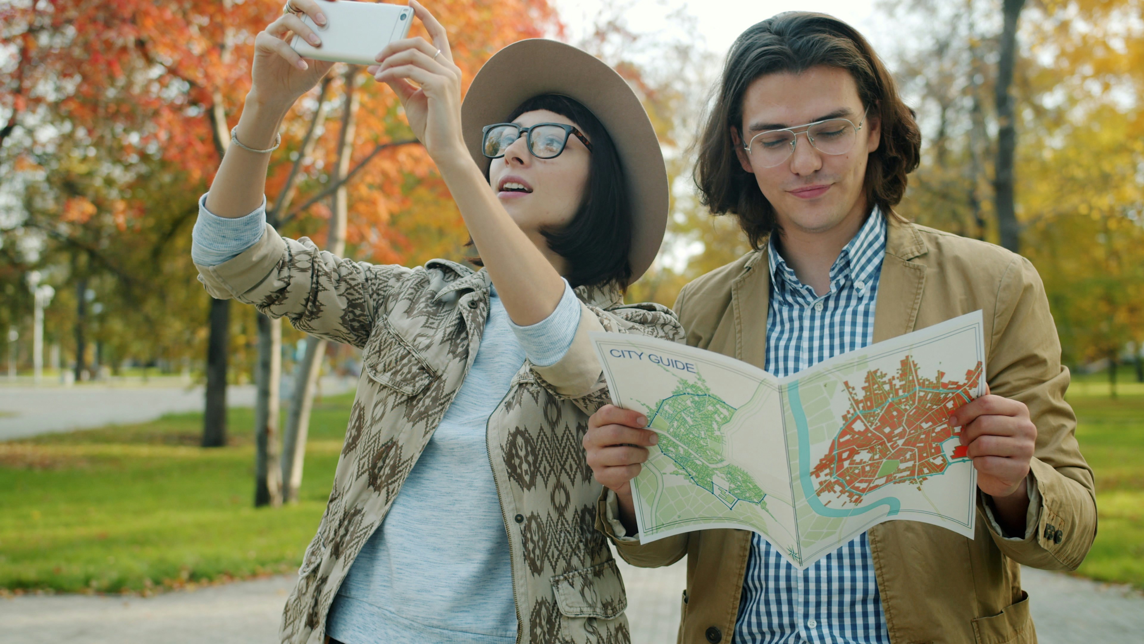 Couple looking at map and taking selfie in autumn park