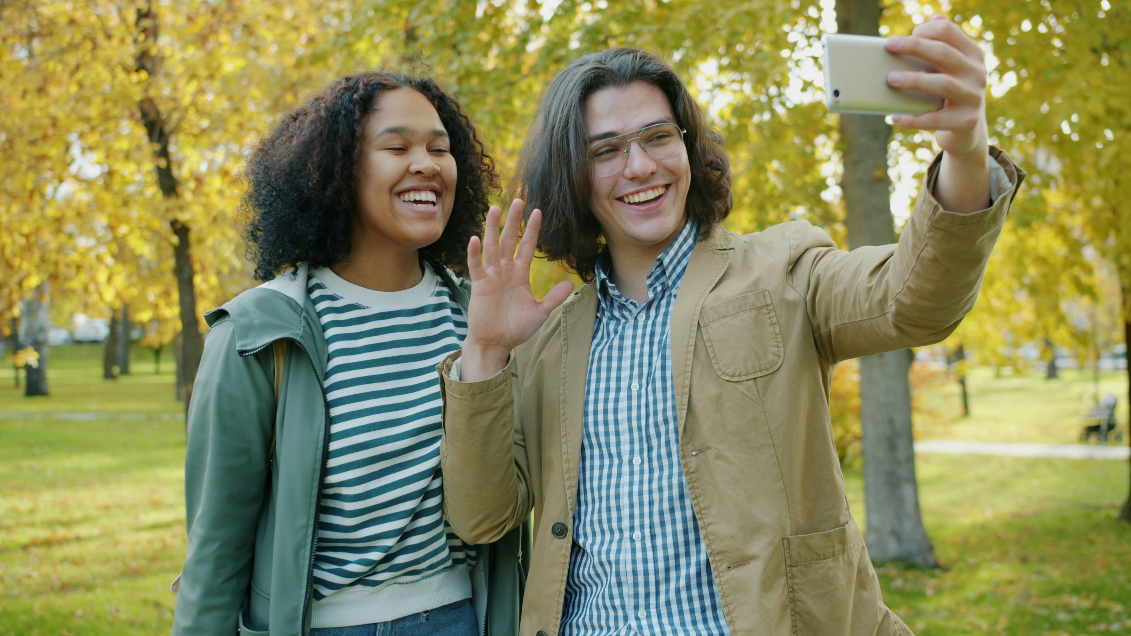 Two people smiling and taking a selfie in an autumn park