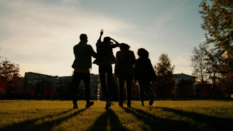 Silhouettes of four friends walking in a park at sunset.