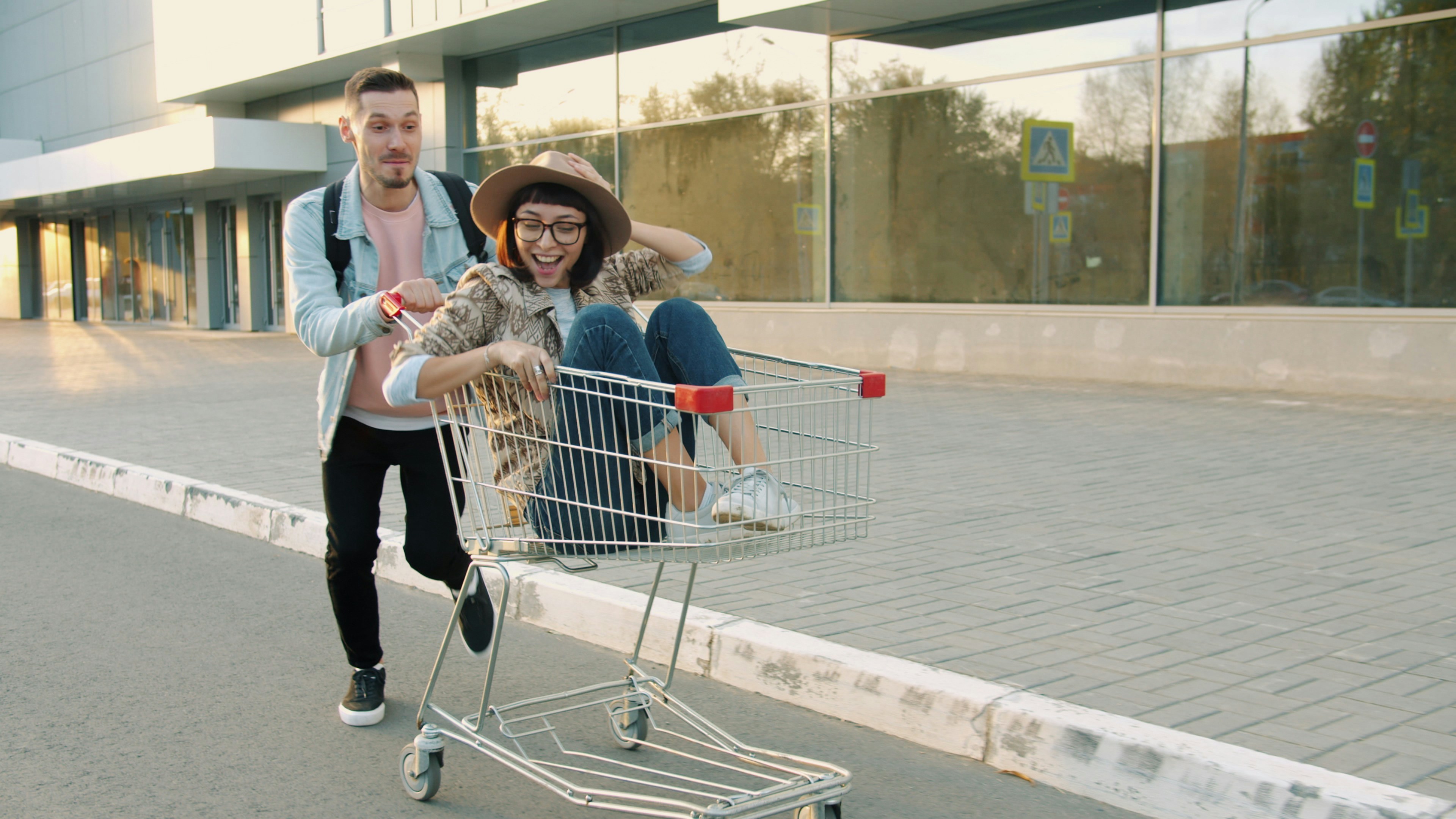 Man pushes woman in shopping cart outside building