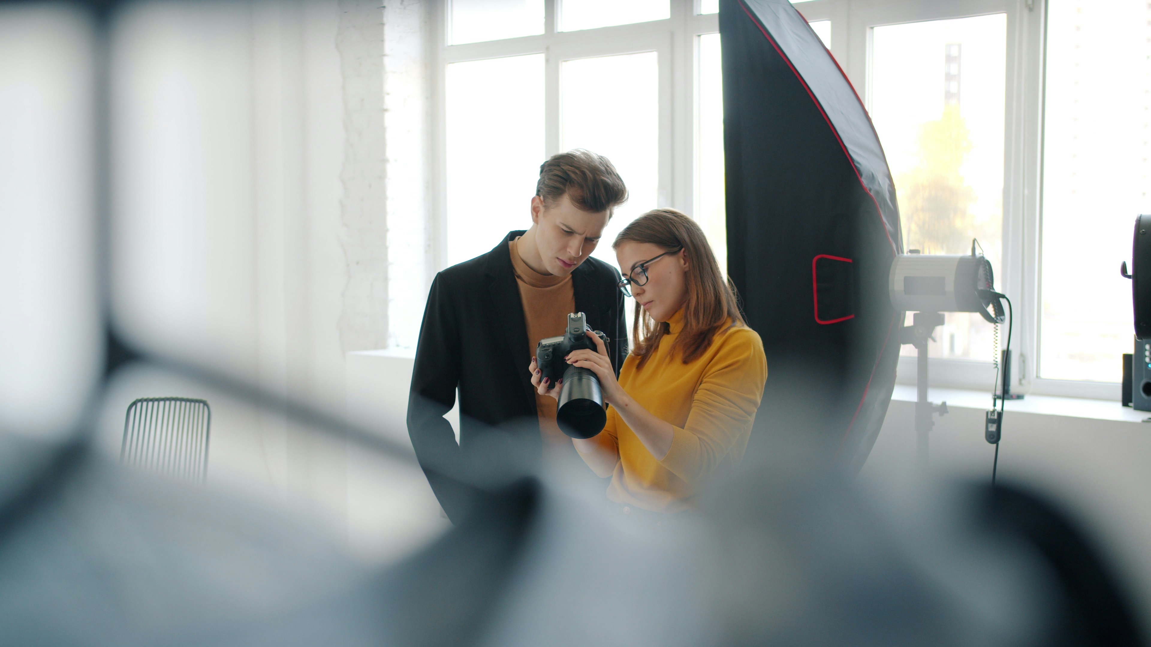 Girl and guy model are talking in photo studio watching pictures on digital camera standing indoors together communicating after photo shoot