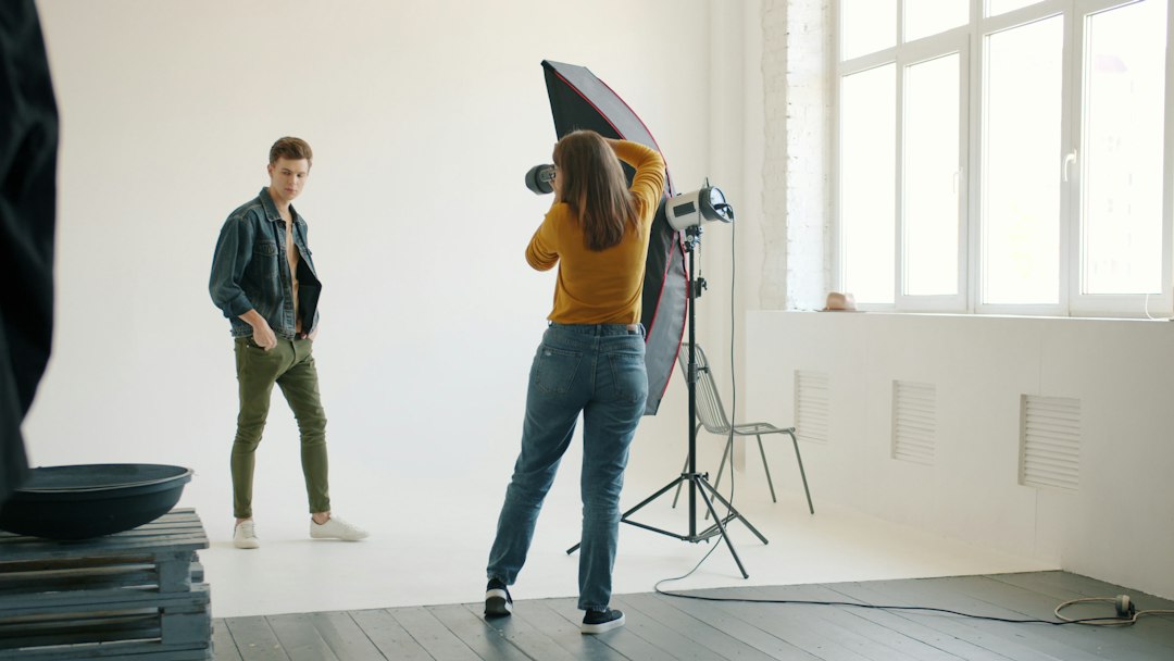 Good-looking young man is posing for photo camera in studio advertising trendy clothes busy with professional photographer. Modern people and photography concept.