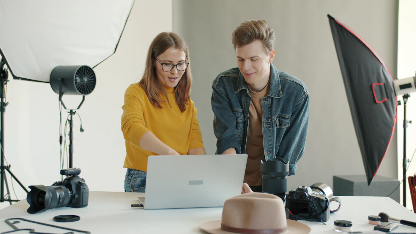 Two people reviewing photography work on a laptop together in a studio setting with camera equipment nearby