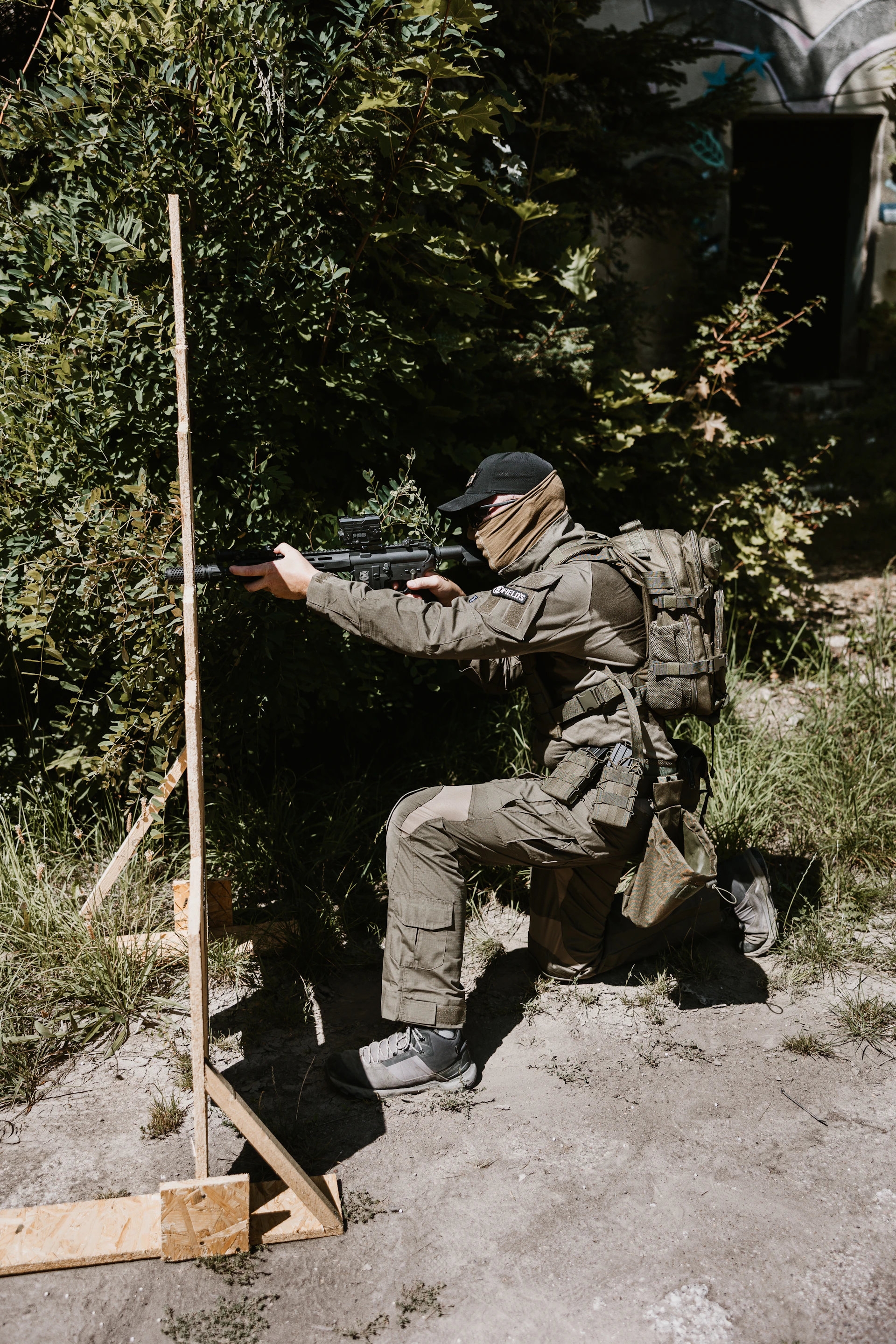 Soldier aiming rifle behind wooden target in foliage.