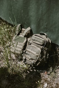 Tactical backpack and vest leaning against camouflage tarp.