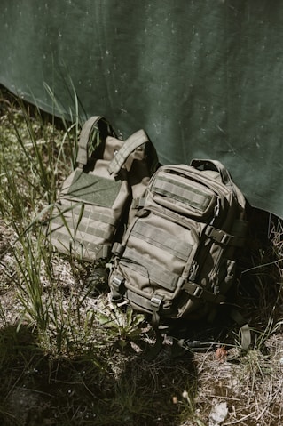 Tactical backpack and vest leaning against camouflage tarp.