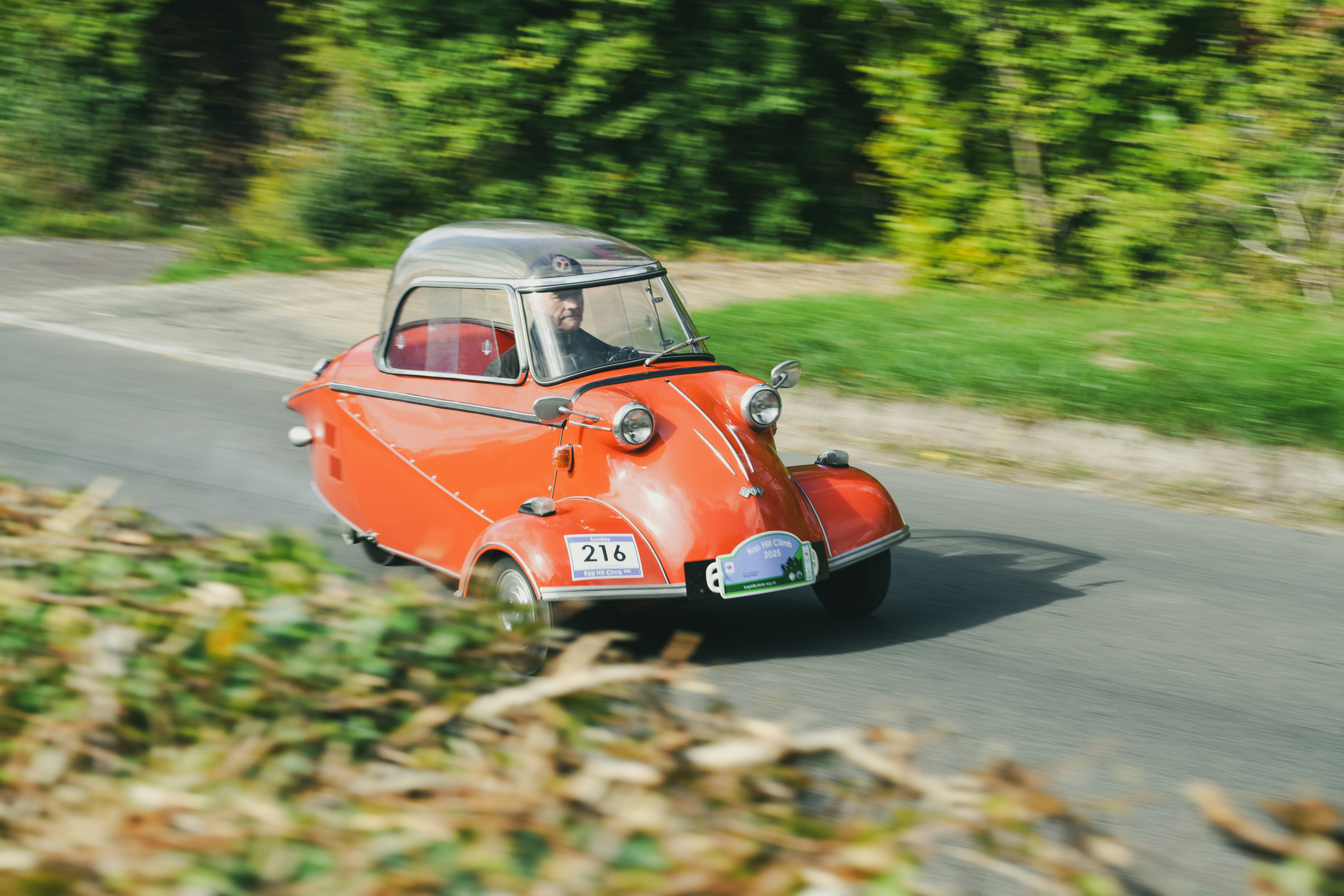 A vintage orange bubble car drives on a country road.