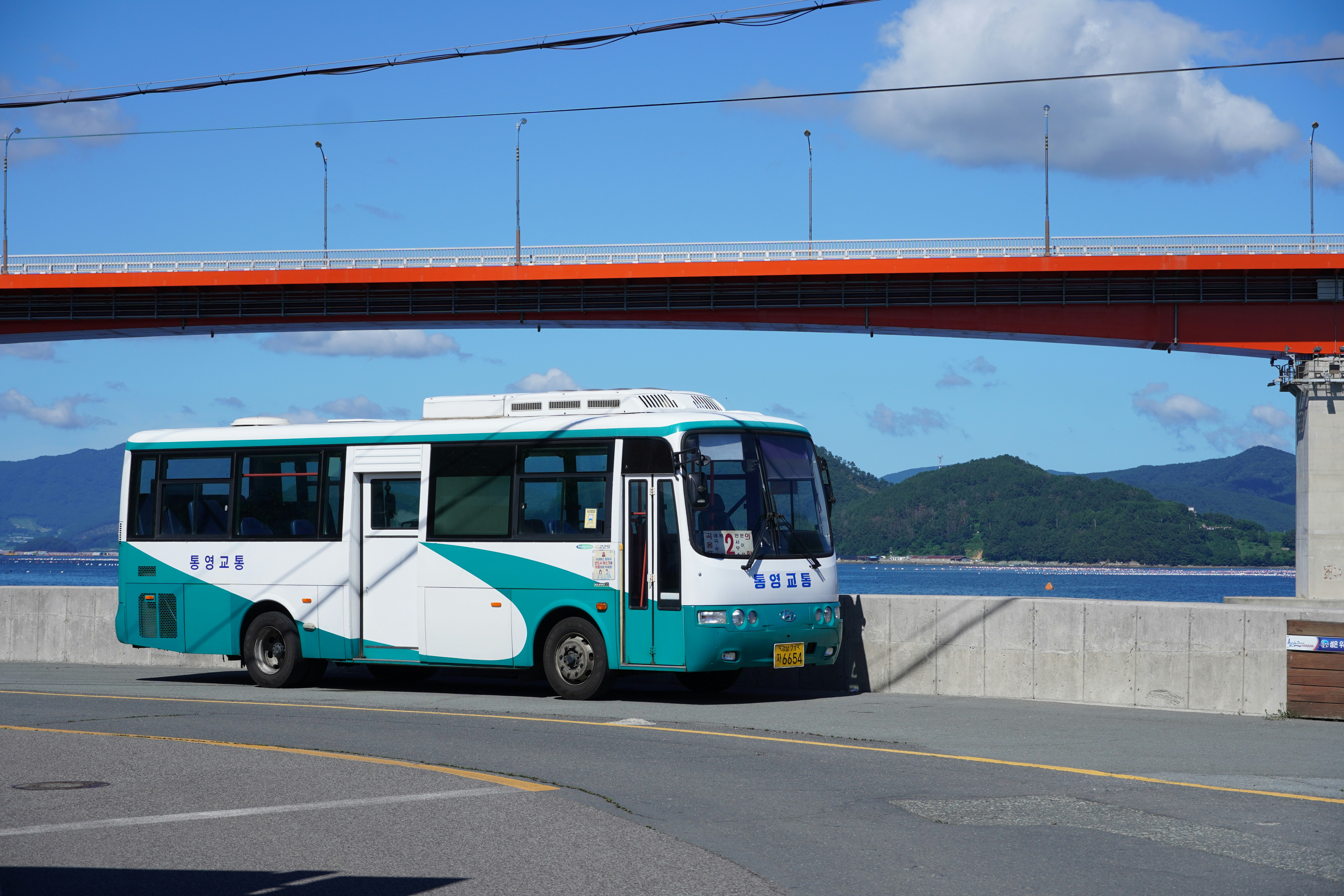 A bus drives under a large orange bridge.