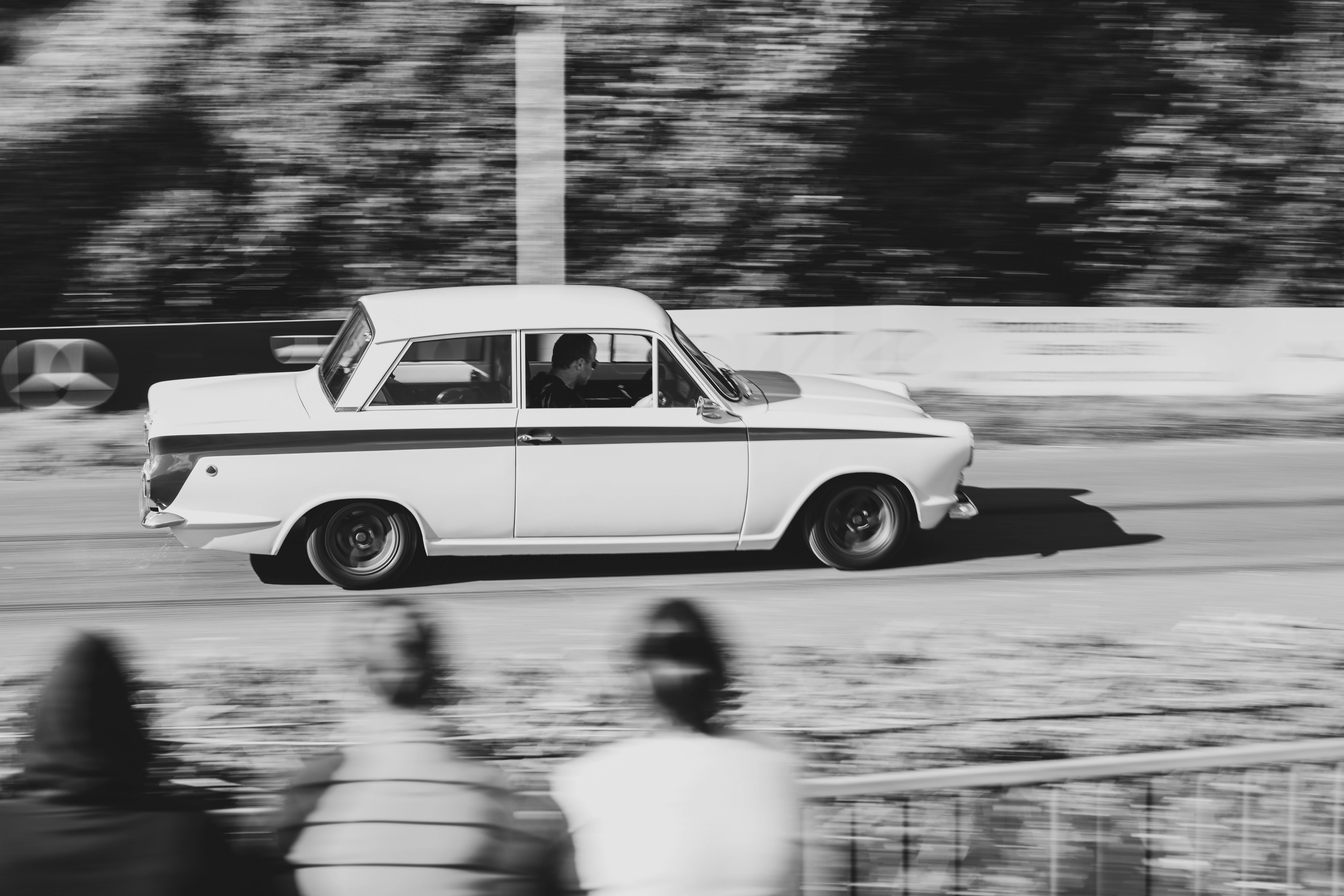Vintage white car racing down a track with blurred spectators.
