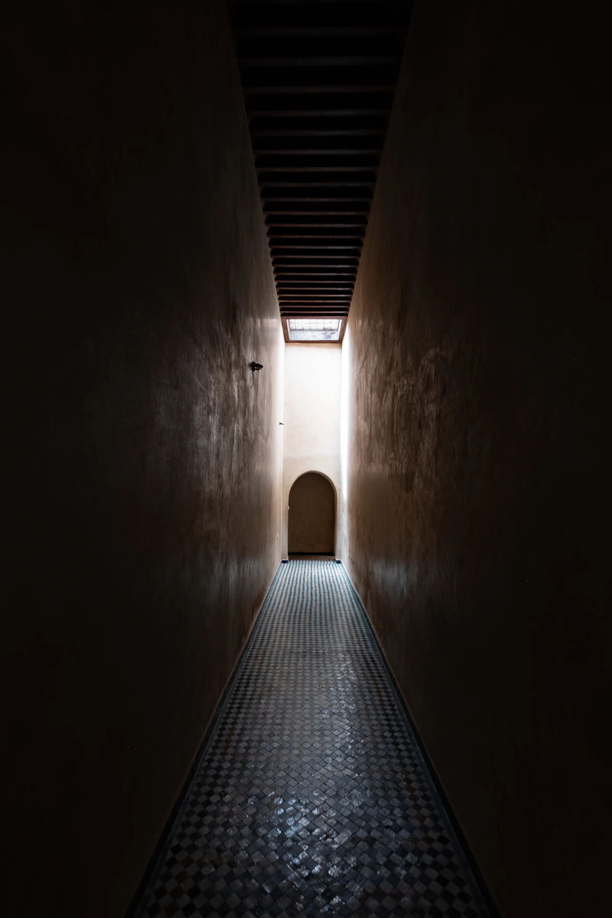 Dim tiled riad hallway in Marrakech, Morocco, leading to a sunlit arched doorway