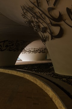 Curved white walls with arabic calligraphy under a bridge.