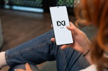 Person holding a smartphone with a logo on screen.
