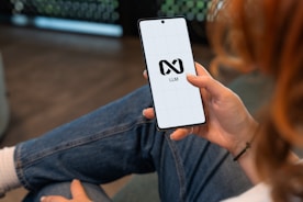 Person holding a smartphone with a logo on screen.