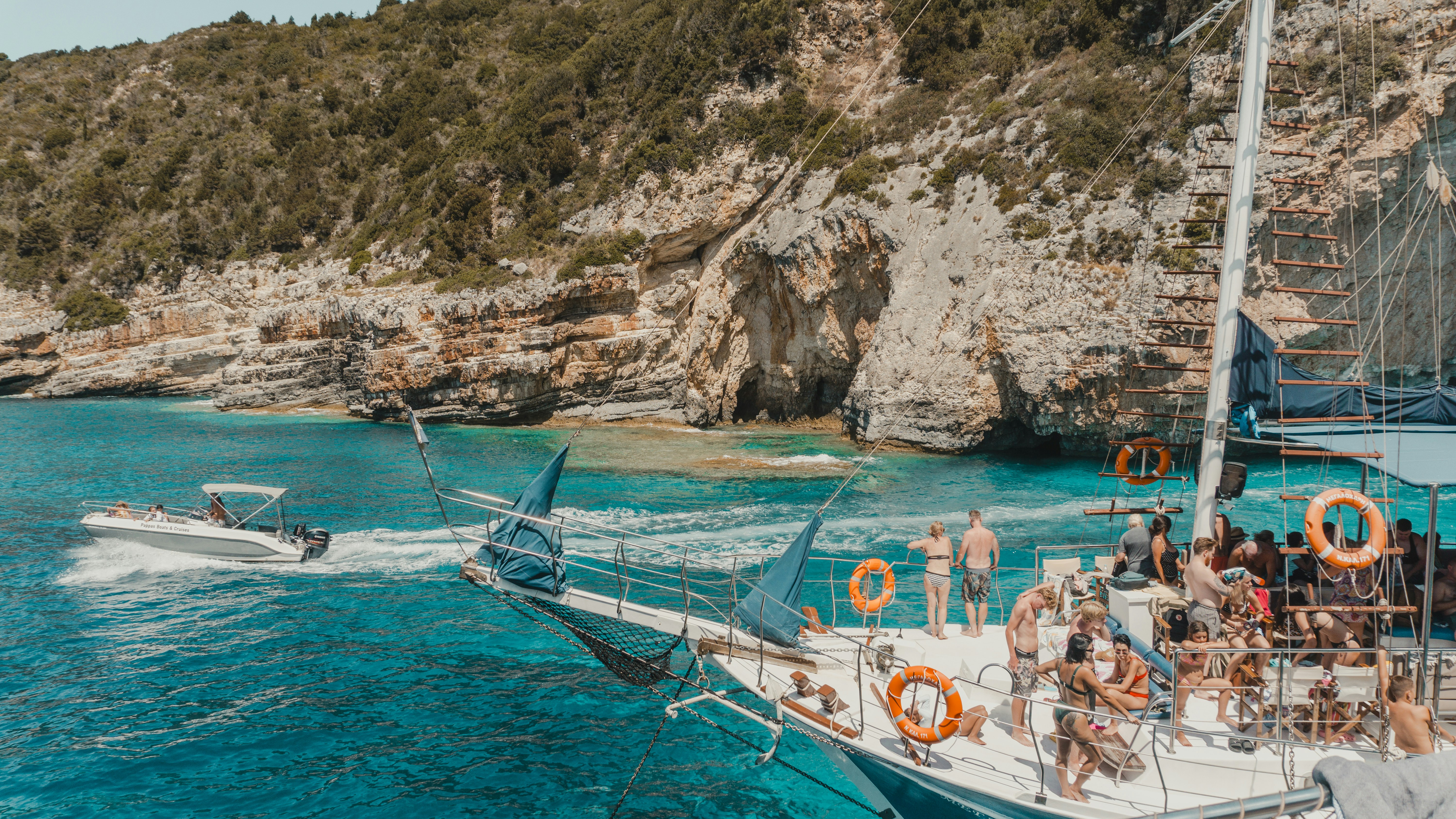 Sailboat anchored near rocky coastline with people relaxing.