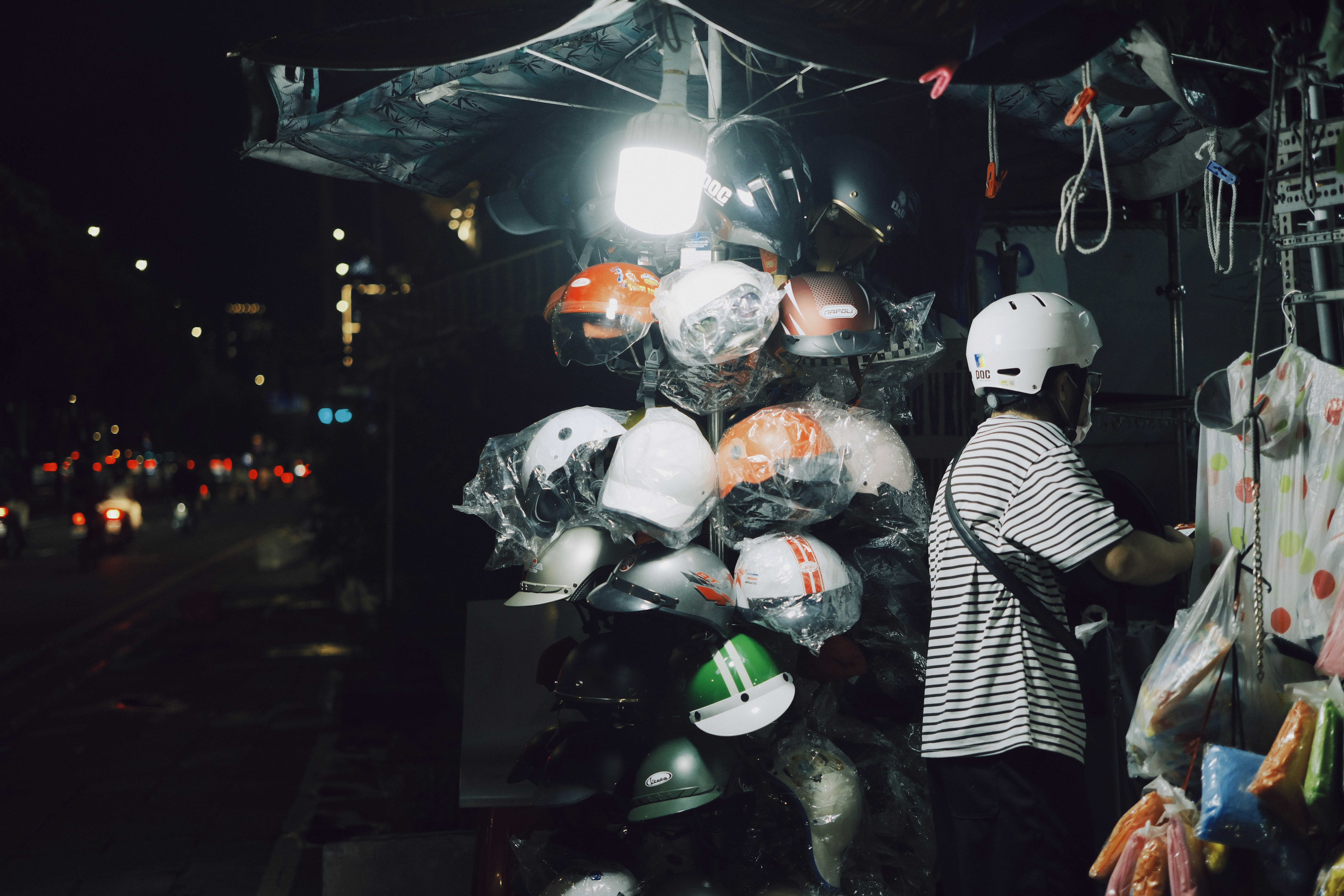 Vendor selling helmets at a night market stall.