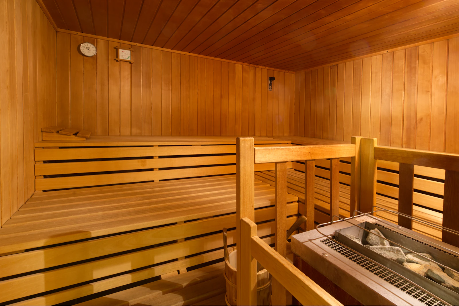 Tiered pine benches in an empty sauna, the stove and its heater stones visible at the right