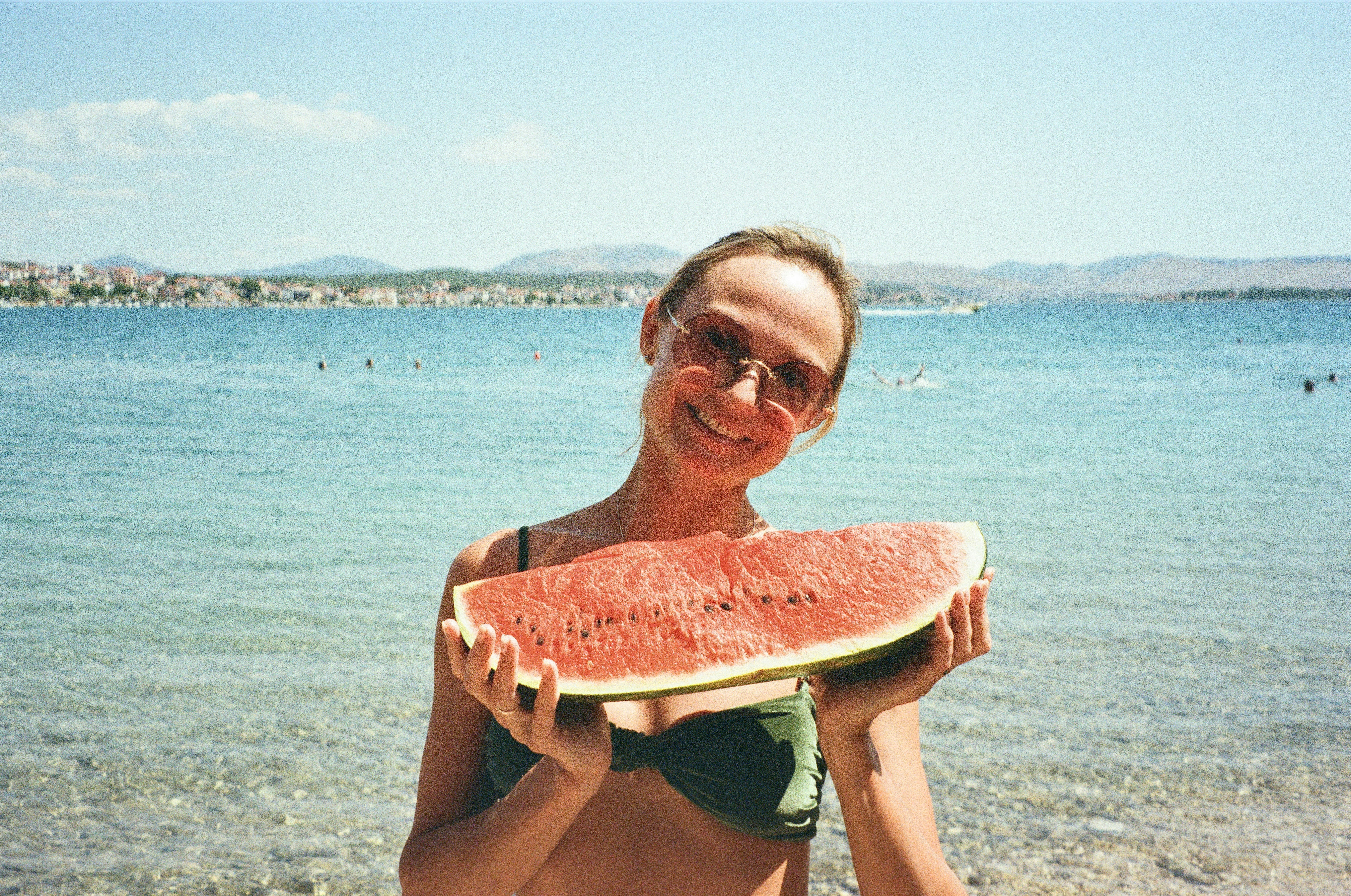 Woman holding a slice of watermelon by the sea