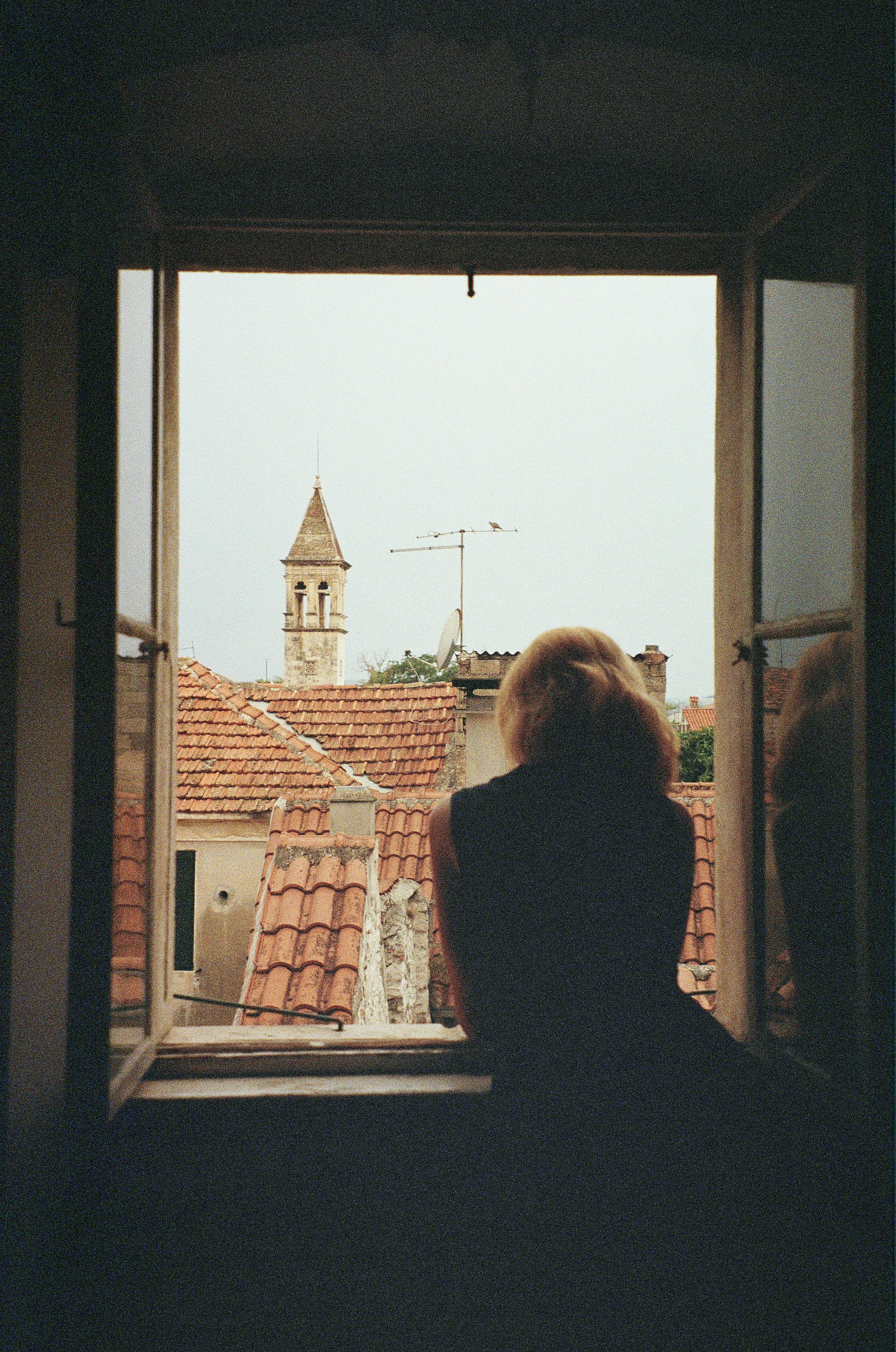 Woman looking out a window at rooftops and tower.