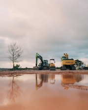 Construction excavators reflected in muddy water under cloudy sky