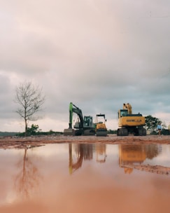 Construction excavators reflected in muddy water under cloudy sky