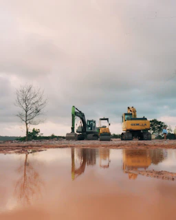 Construction excavators reflected in muddy water under cloudy sky