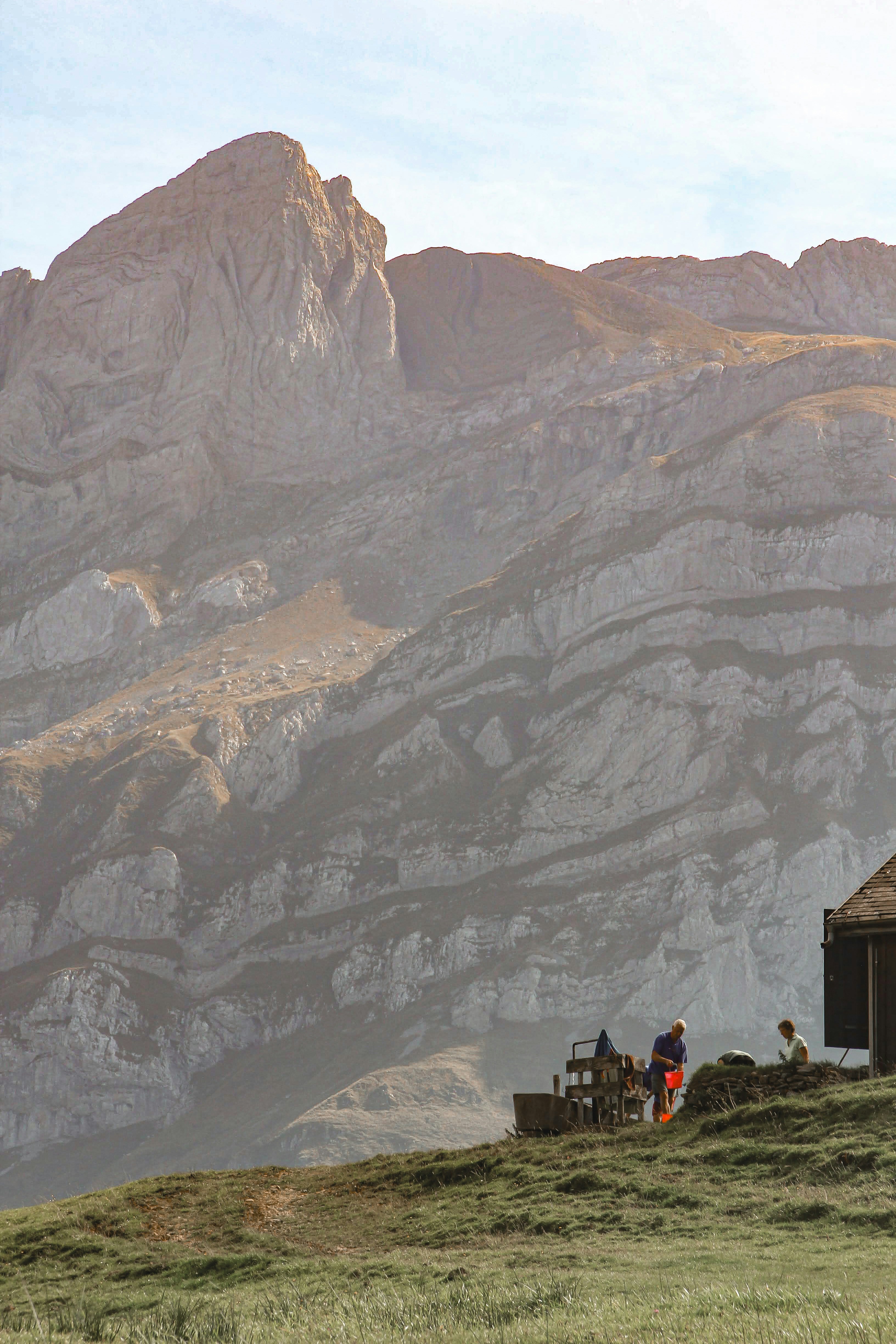People near a building on a grassy hill with mountains.