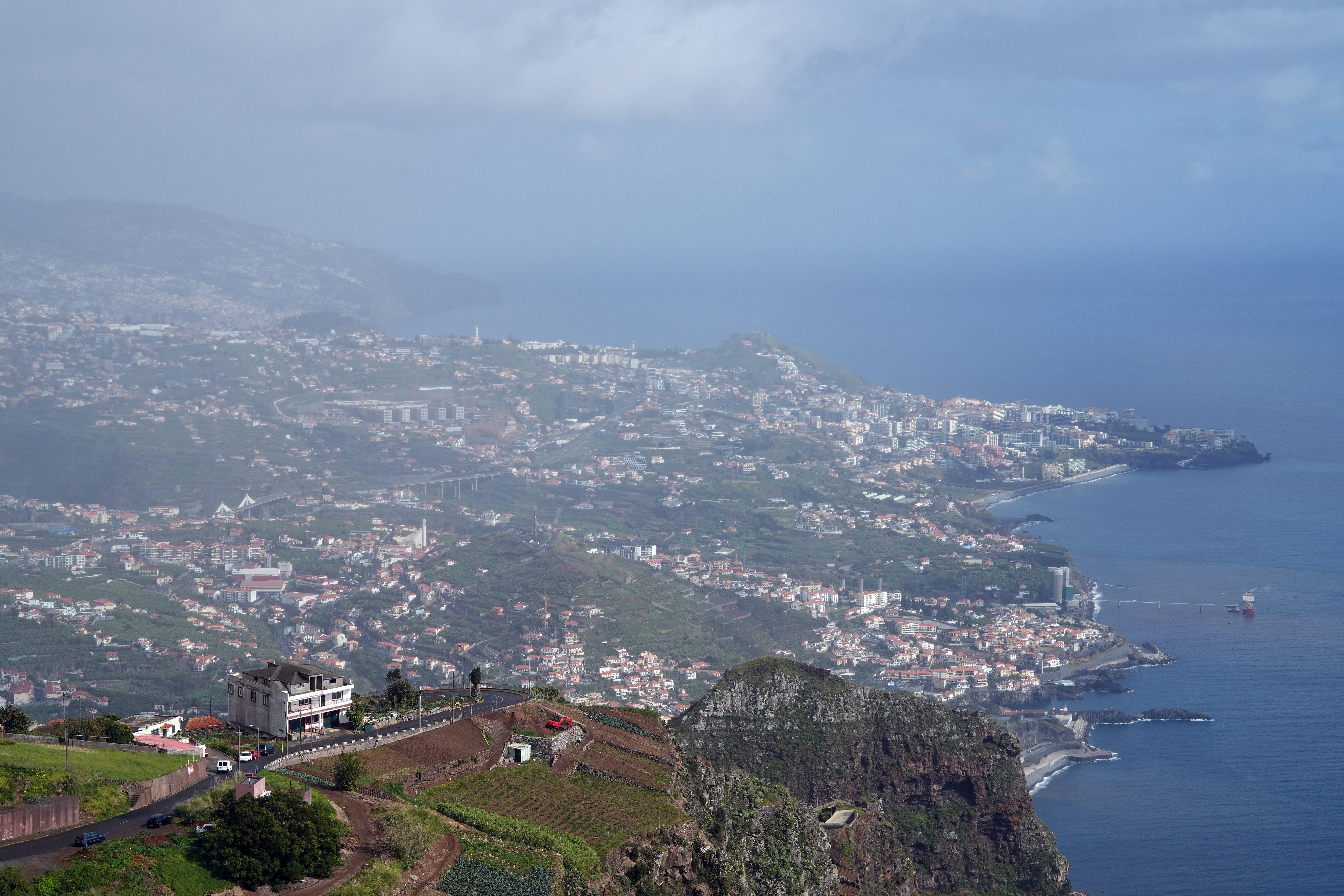 coastal city nestled on steep, green hills overlooking ocean.