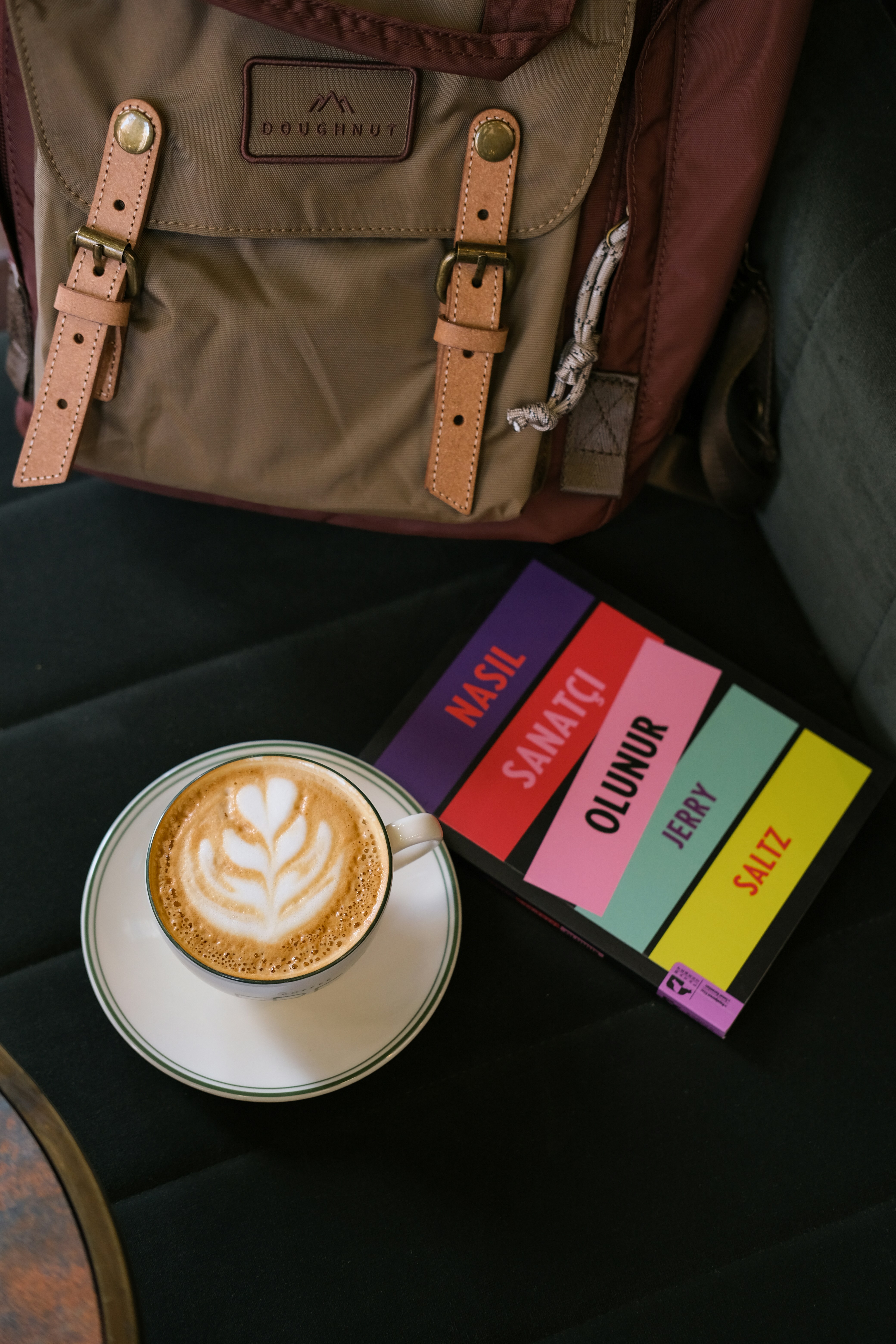 Latte art coffee next to a book and backpack