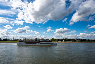 A modern yacht sails on a wide river under clouds