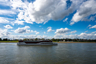 A modern yacht sails on a wide river under clouds