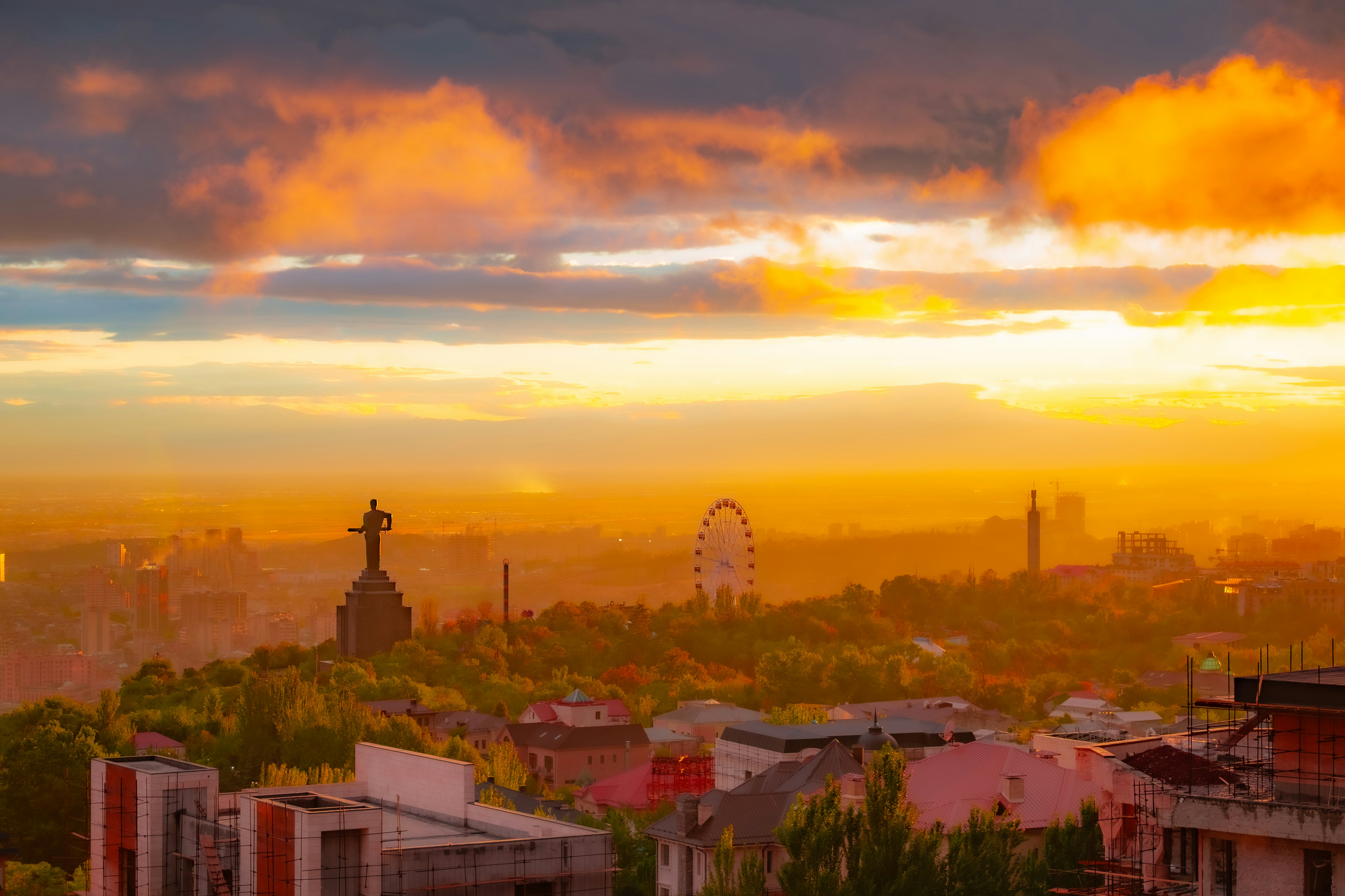 Tramonto dorato sullo skyline di una città con ruota panoramica in lontananza.