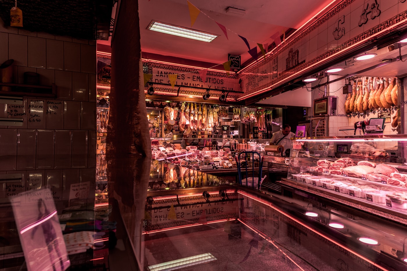 A butcher shop counter lit by pink and red neon signage
