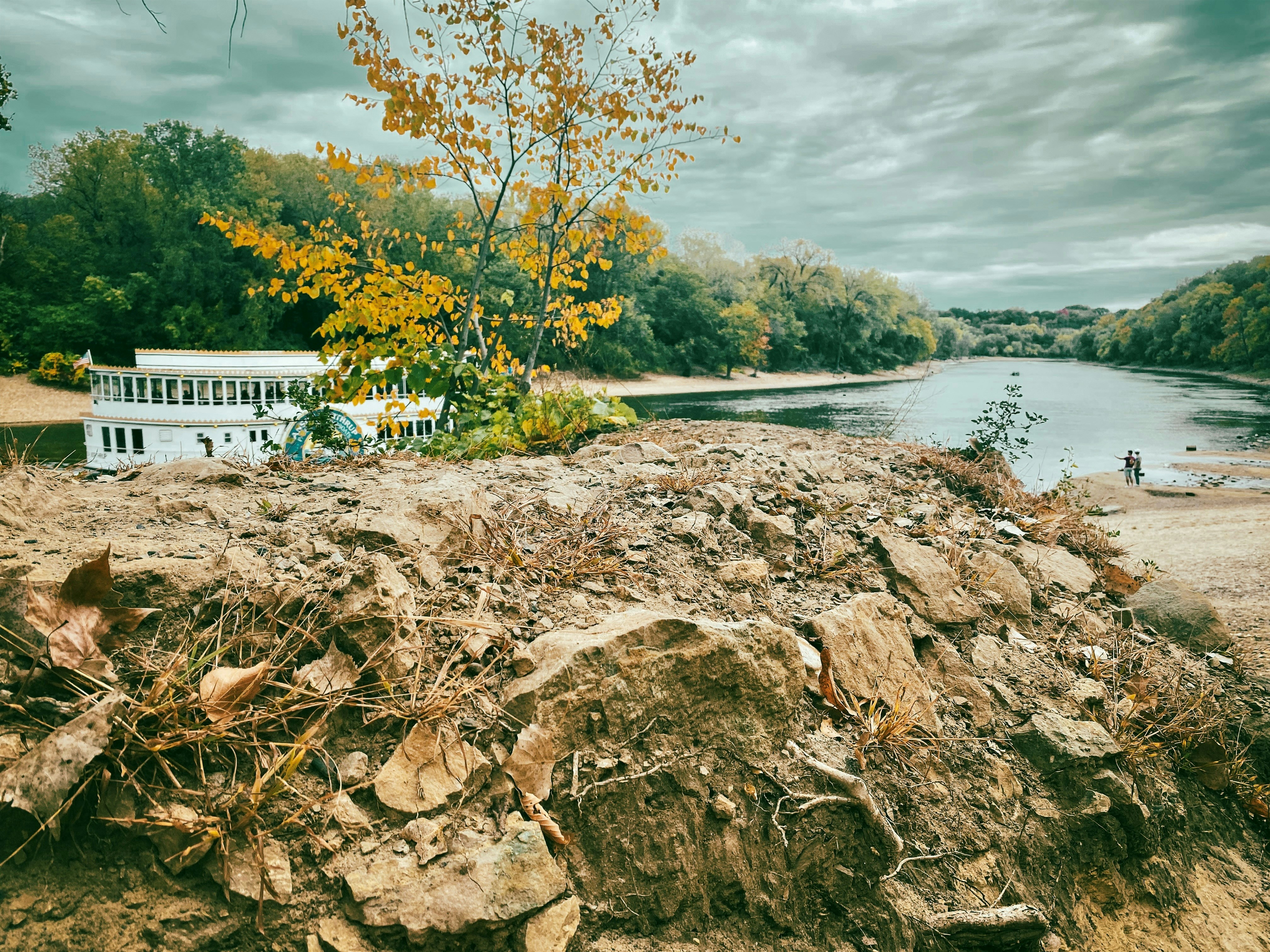Autumn foliage by a calm river with a white building.