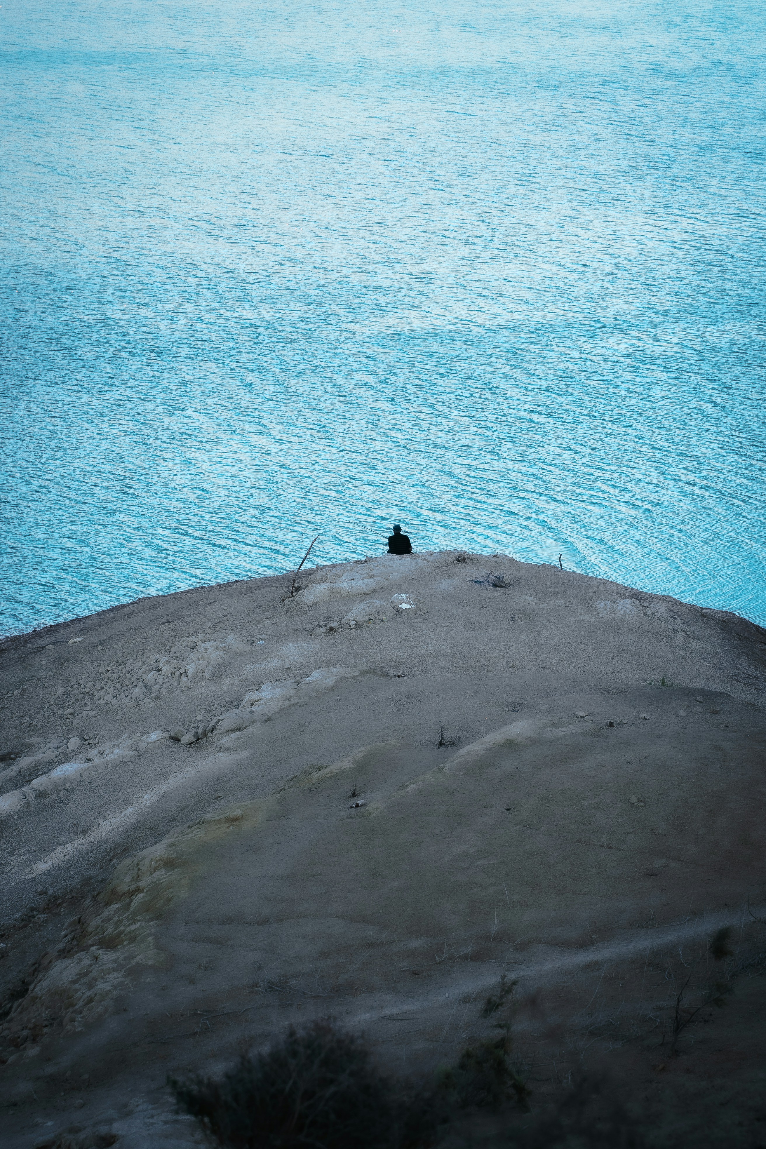 A lone figure sits on a hill overlooking the ocean.
