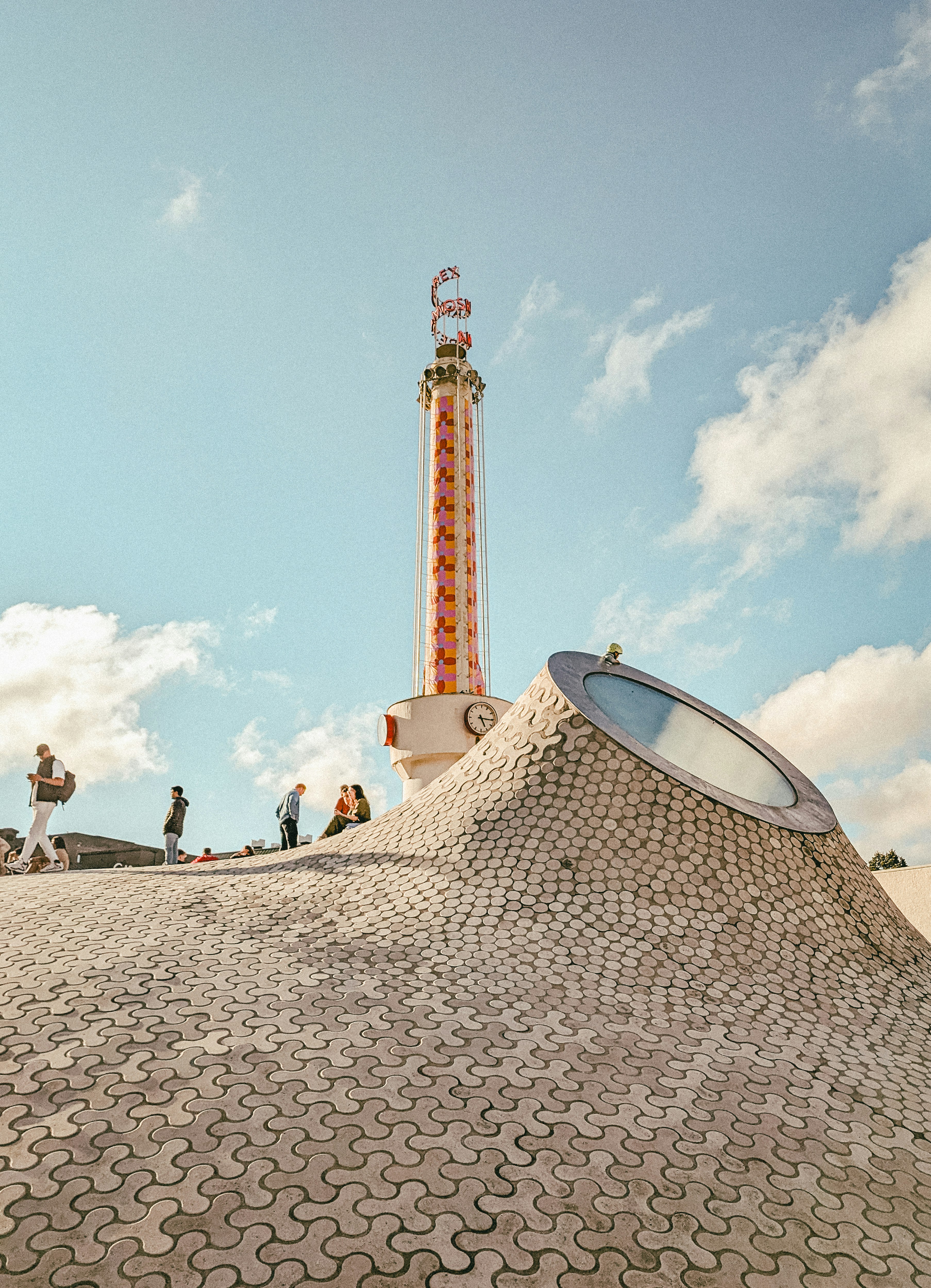People relax near a tall amusement park tower.