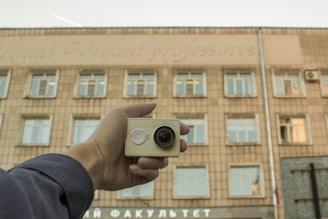 Hand holding small camera in front of building