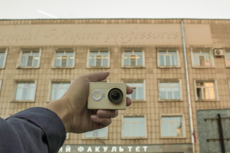Hand holding small camera in front of building