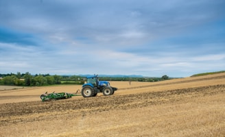Blue tractor plowing a field under a cloudy sky