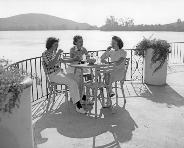 Three women sitting at a table by the water.