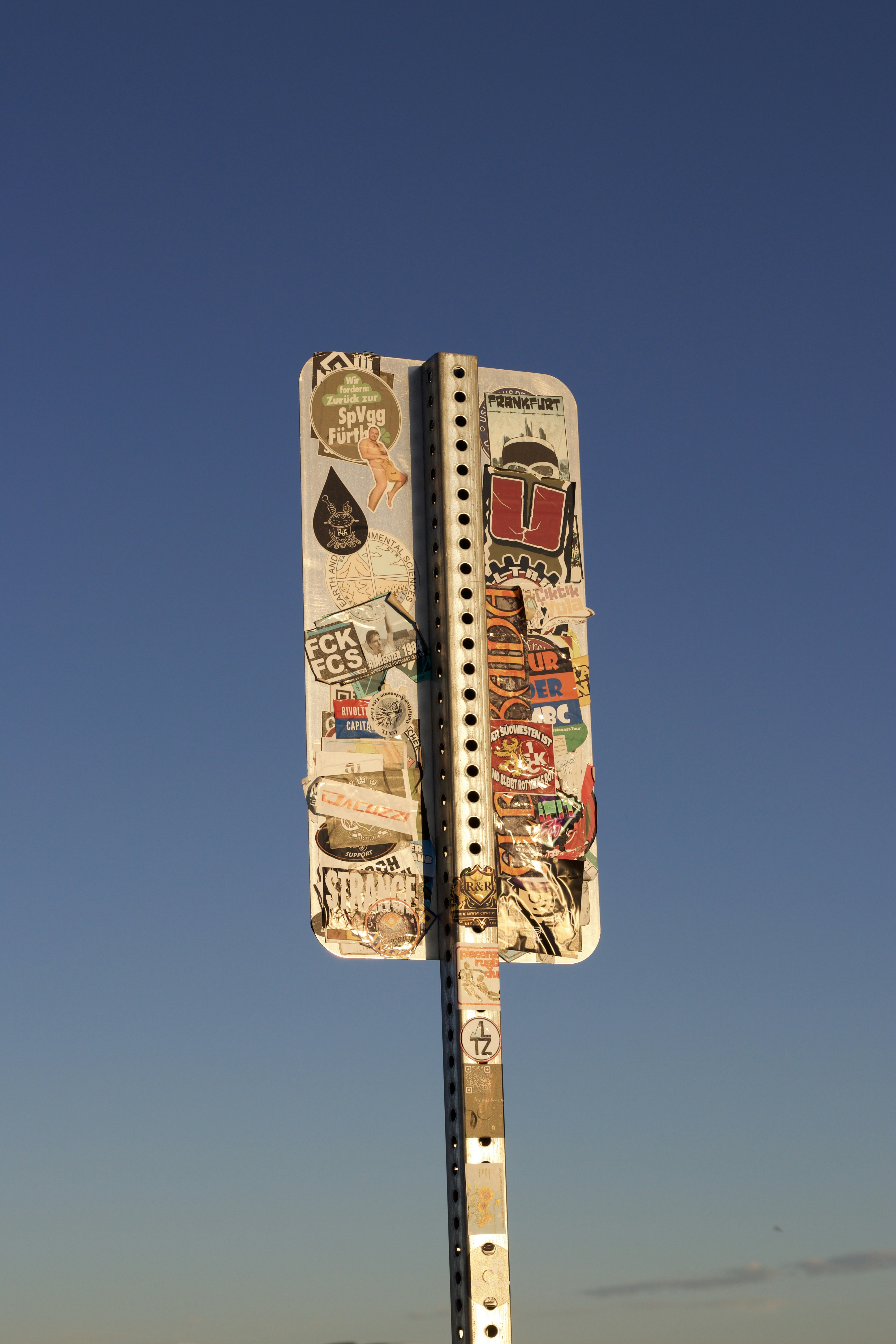 Street sign covered in stickers against blue sky