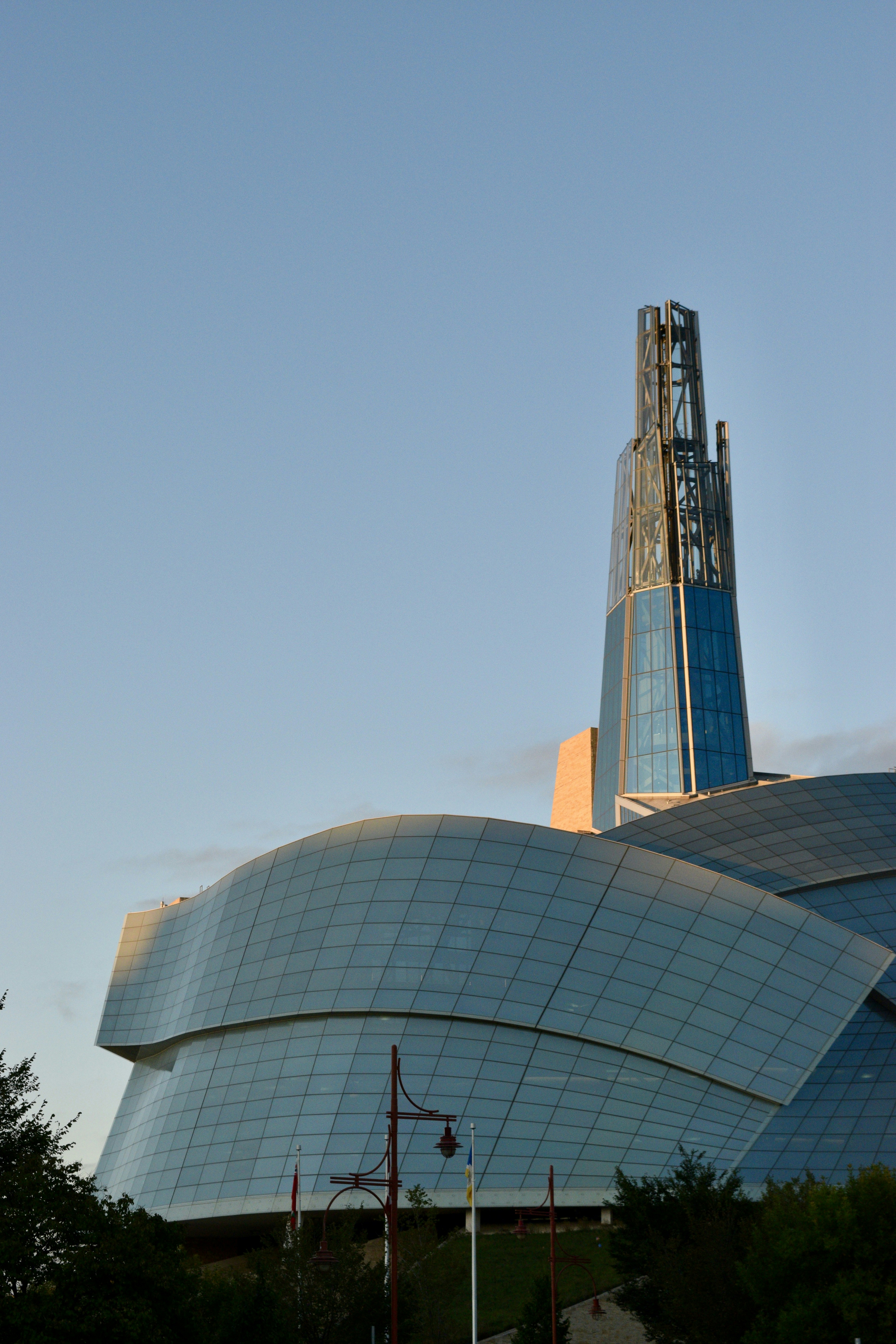 Modern glass building with a tall spire against blue sky
