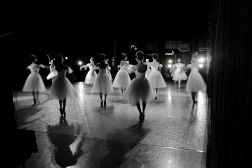 Motion-blurred group of dancers in white tutus mid-performance on stage