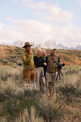 Four people observe mountains from a grassy field.