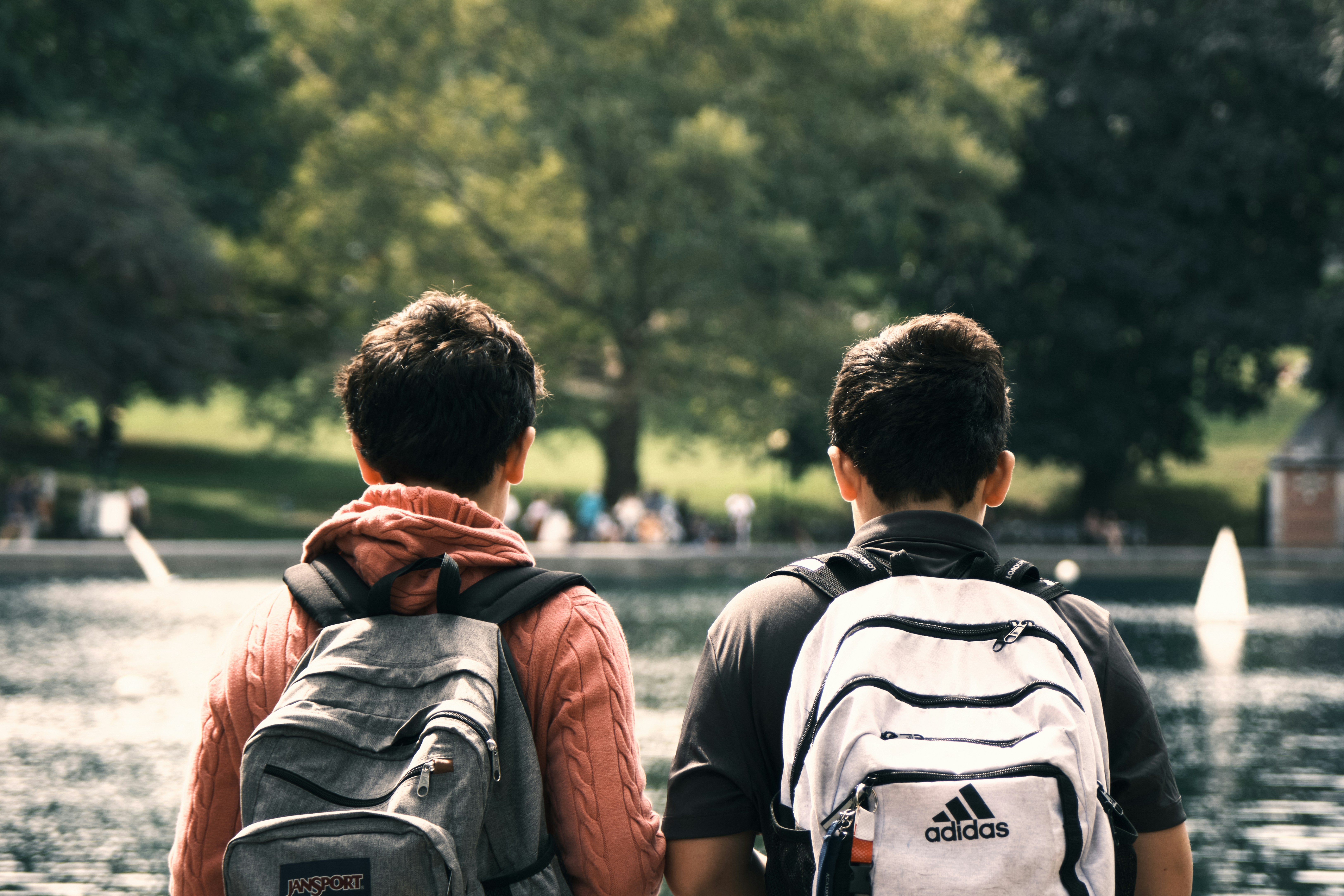Two friends with backpacks look at a lake.