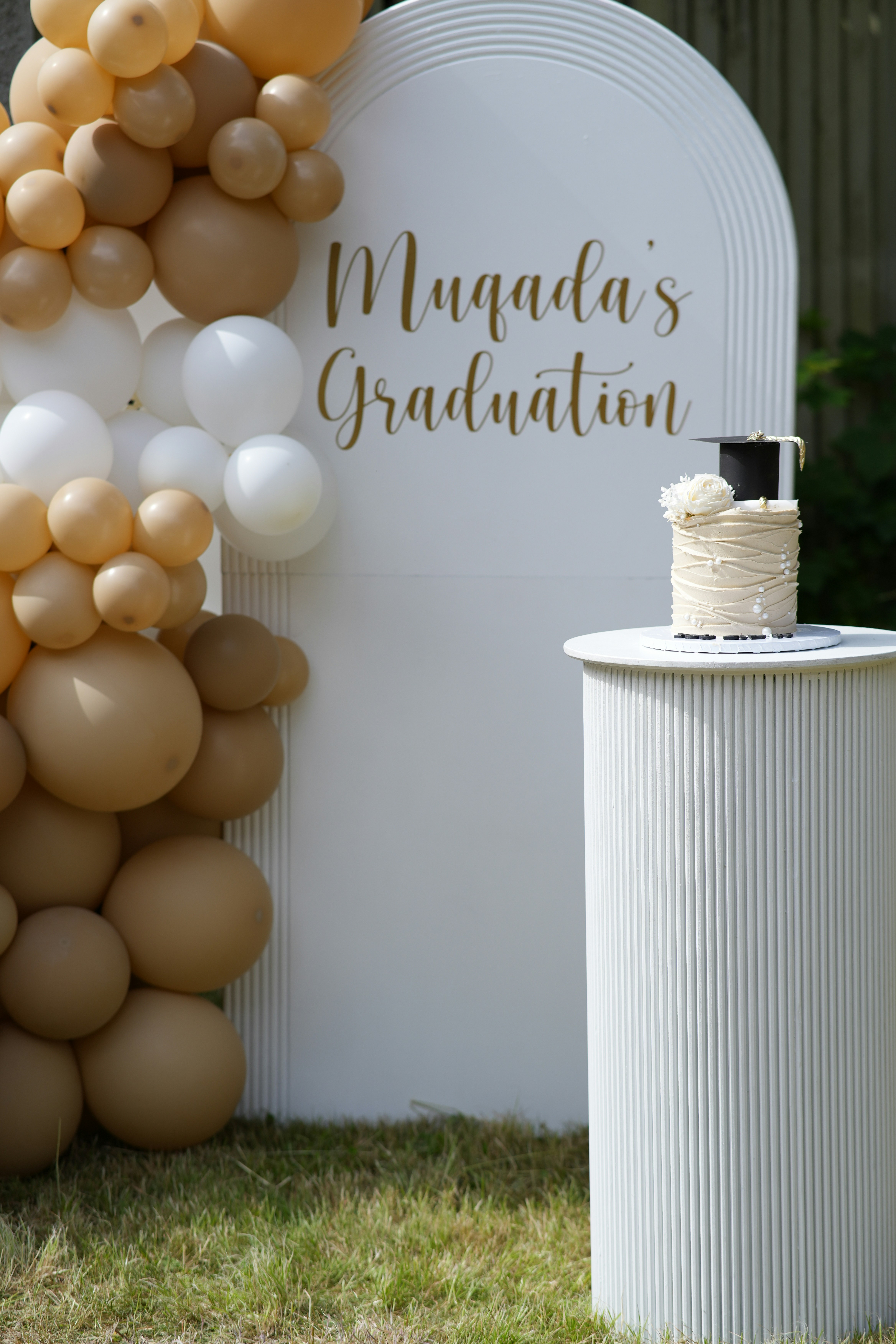 Graduation party setup with neutral balloons, graduation backdrop and celebration cake